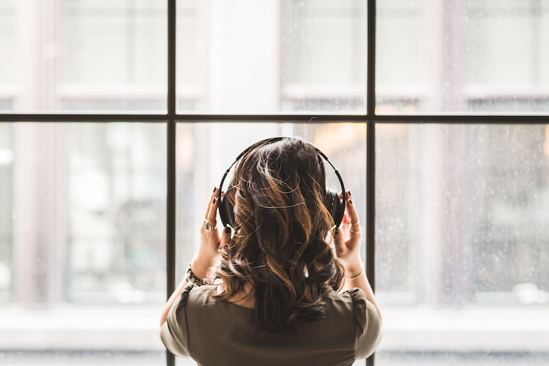 Woman wearing headphones over wavy hair, looking out the window, image used for Ari Monkarsh blog about podcasts for entrepreneurs