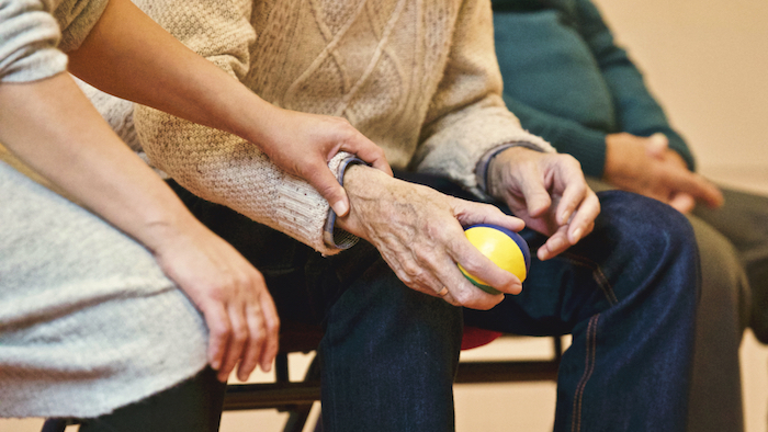 Two people sitting together, one older and holding a stress ball, the other holding the older man's hand, image used for Ari Monkarsh post about supporting a loved one struggling with depression